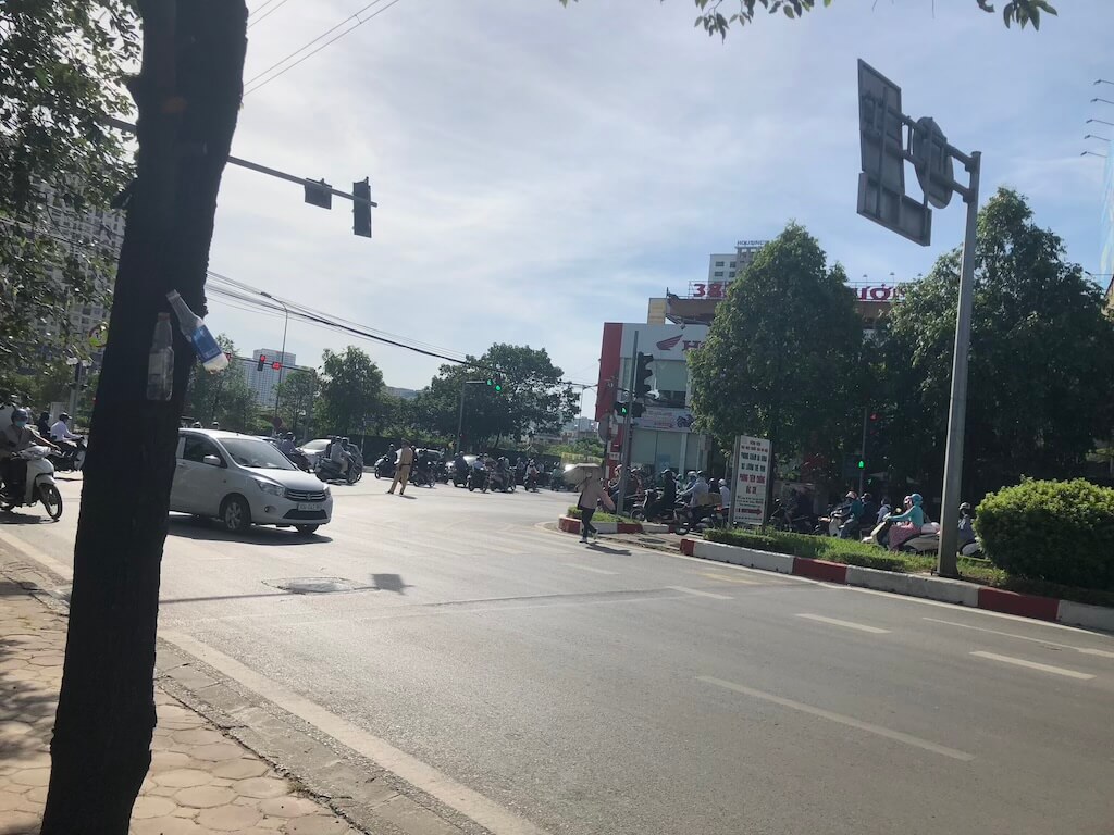 強い直射日光が道路を照らすベトナムの街角の風景。暑さの中、多くのバイクや車が交差点を行き交う日常的な街中の様子。