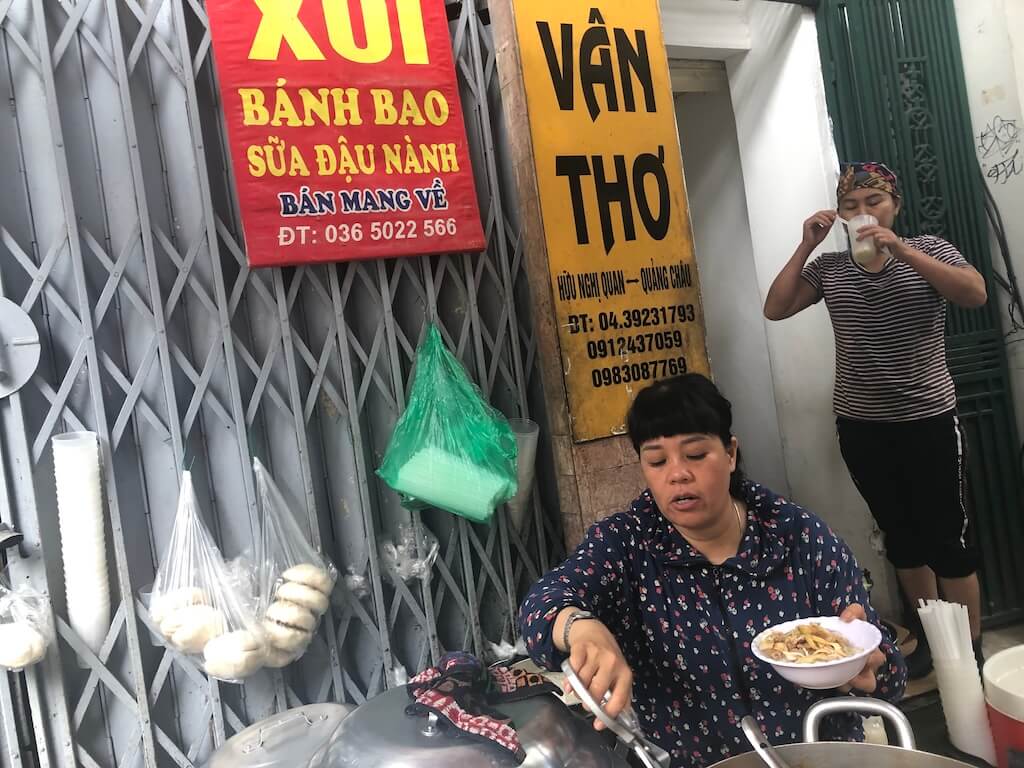 ハノイ旧市街の路上で、朝食のおこわ（Xôi）を販売する屋台。北部の素朴ながらも活気ある朝の食文化と人々の生活感。