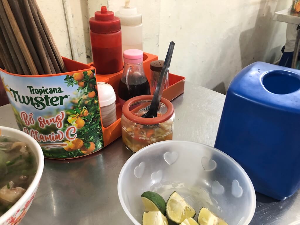 ハート柄のボウルに入ったカットライムや、箸立て、調味料ボトルが並ぶローカルのフォー屋のテーブル